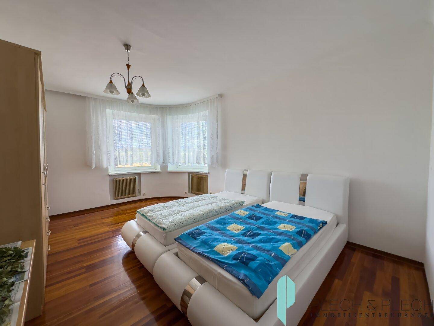 Schlafzimmer mit zwei Betten, dunklem Parkettboden und großen Fenstern.