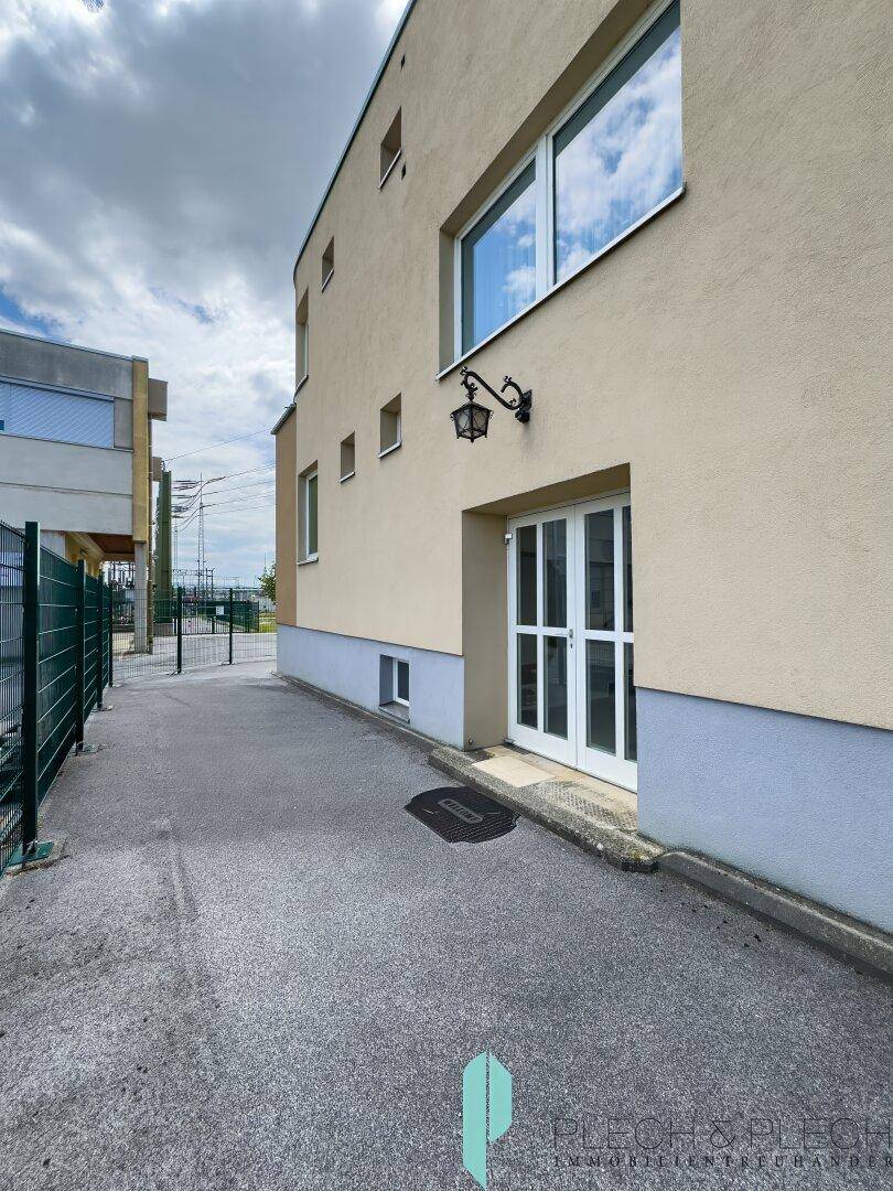 Seitenansicht des Gebäudes mit Zugangstür und gepflastertem Weg.