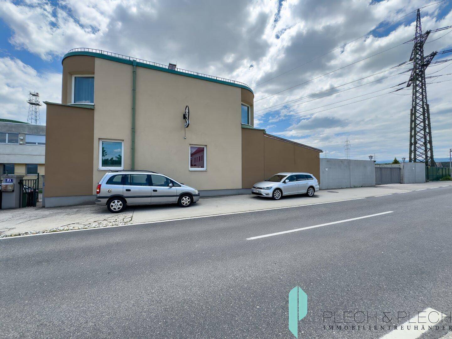 Gebäudeansicht von der Straße mit parkenden Autos und Strommasten im Hintergrund.