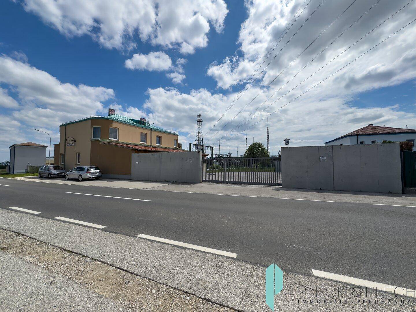 Gesamtansicht des Gebäudes von der Straße mit großem Eingangstor und umliegender Landschaft.