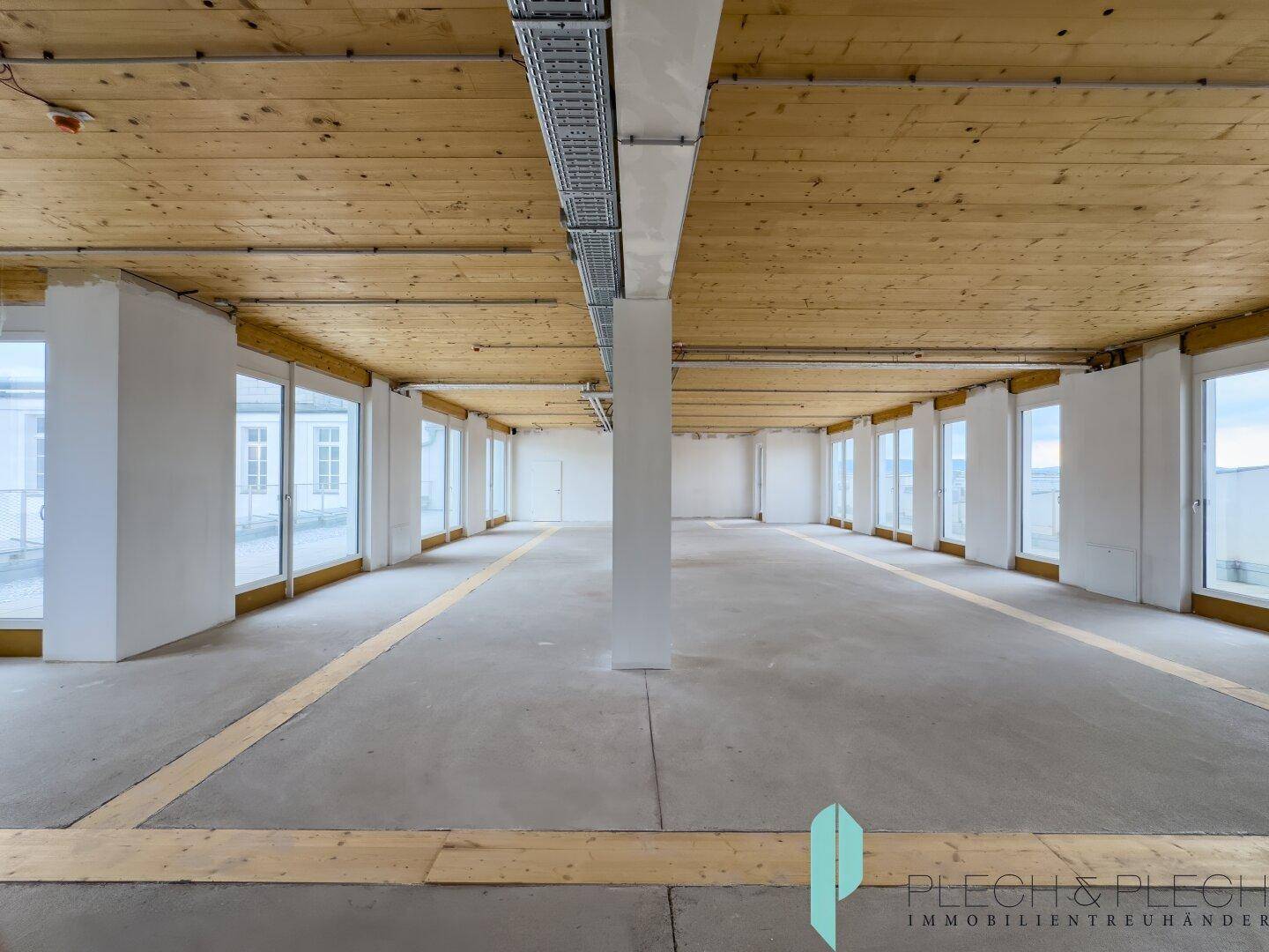 Großer, offener Büroraum mit Holzbalkendecke und vielen Fenstern, bereit für den Ausbau.