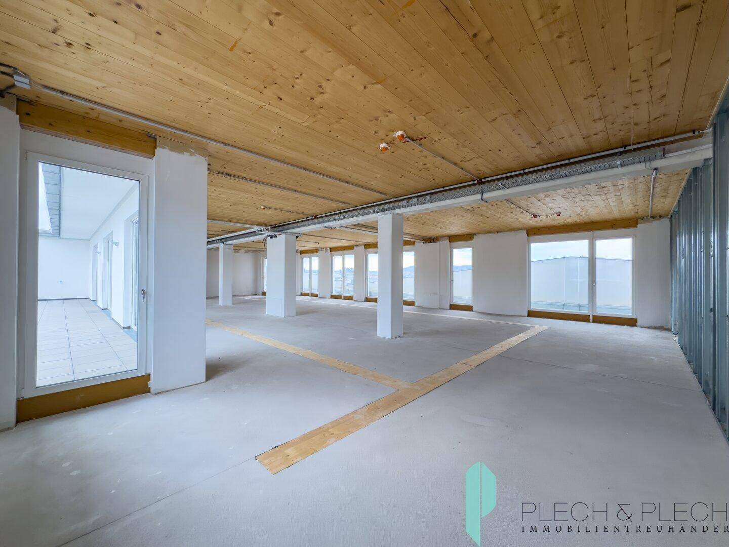 Heller, weitläufiger Bürobereich mit sichtbarer Holzdecke und großen Fensterfronten.