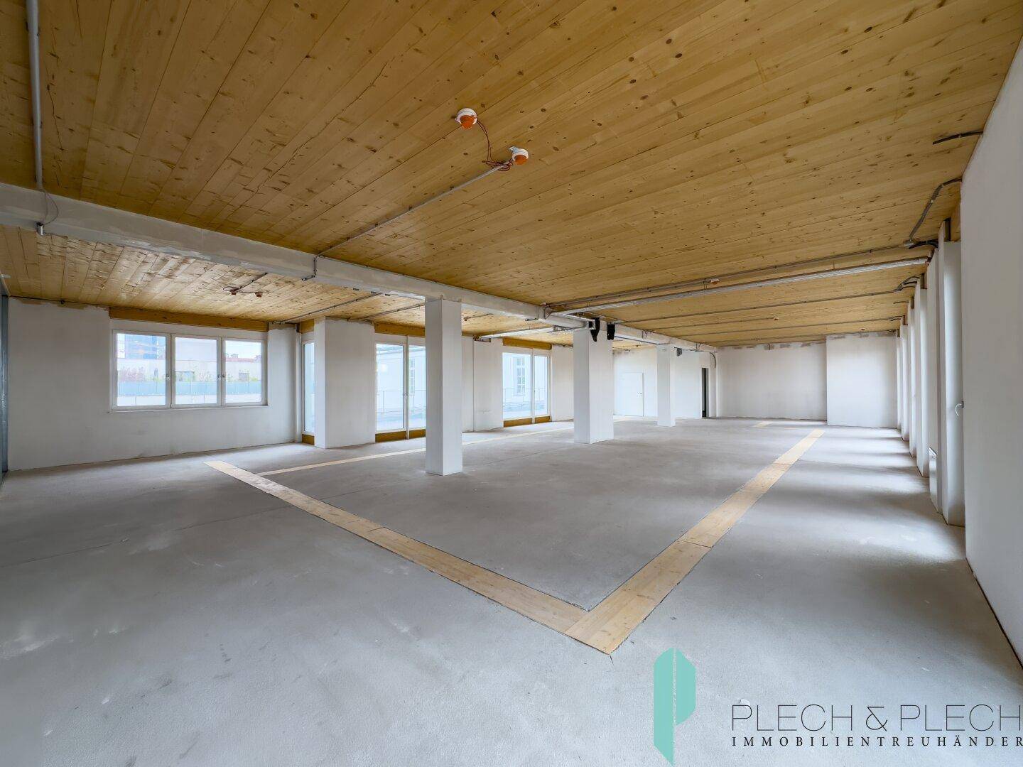 Geräumiger, unmöblierter Büroraum mit Holzbalkendecke und vielen Fenstern, ideal für individuelle Gestaltung.