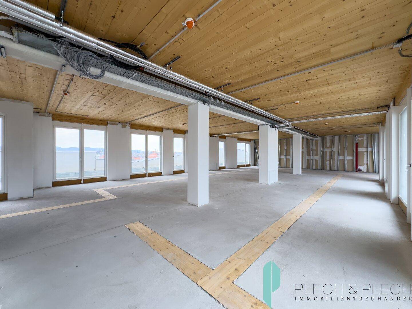 Offener Bürobereich mit Holzbalkendecke, Betonboden und großen Fenstern, bereit für den Innenausbau.