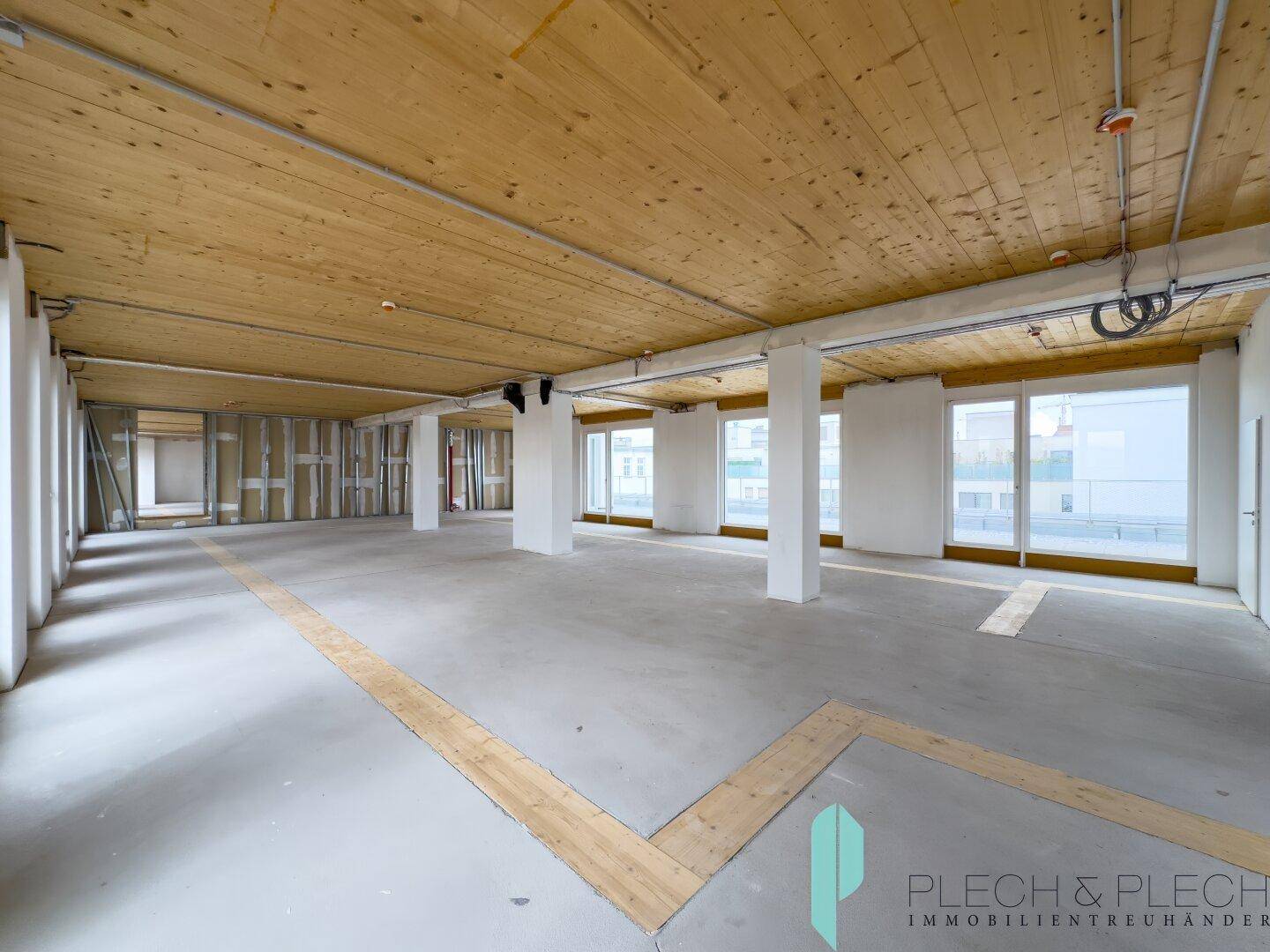 Weitläufiger, heller Büroraum mit Holzbalkendecke und großen Fensterfronten, ideal für flexible Nutzung.