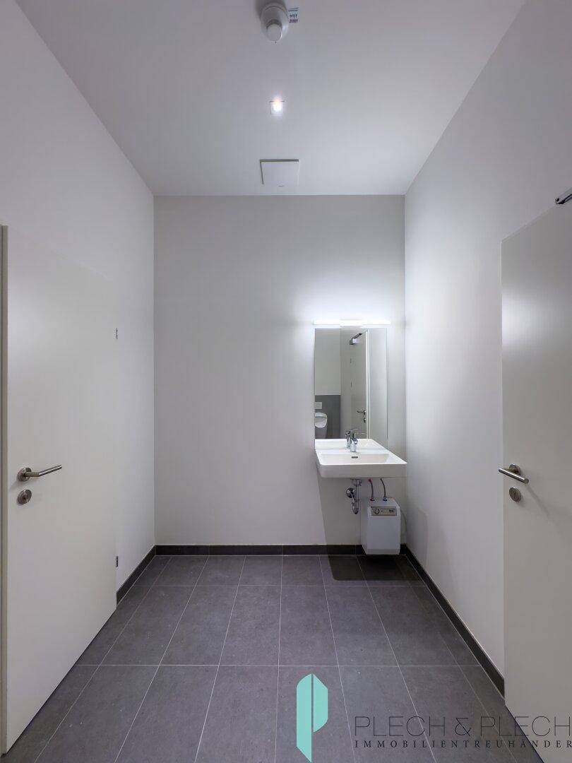 Heller Waschraum mit modernem Waschbecken, Spiegel und grauen Bodenfliesen.