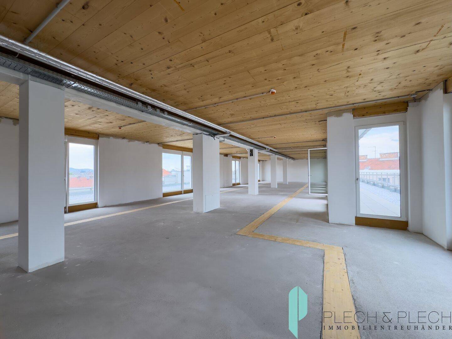 Großer, heller Gewerberaum mit Holzbalkendecke, Betonboden und vielen Fenstern, ideal für Büros oder Studios.