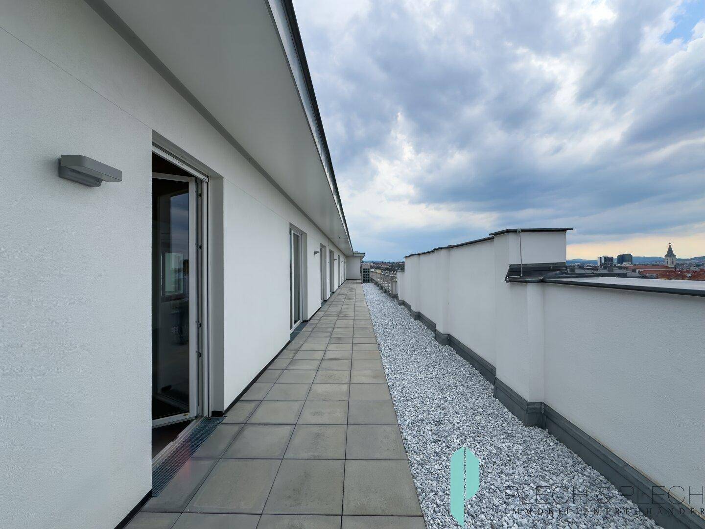 Weitläufige Dachterrasse mit Fliesenboden und Kiesbett, ideal für Entspannung mit Blick auf die Stadt.