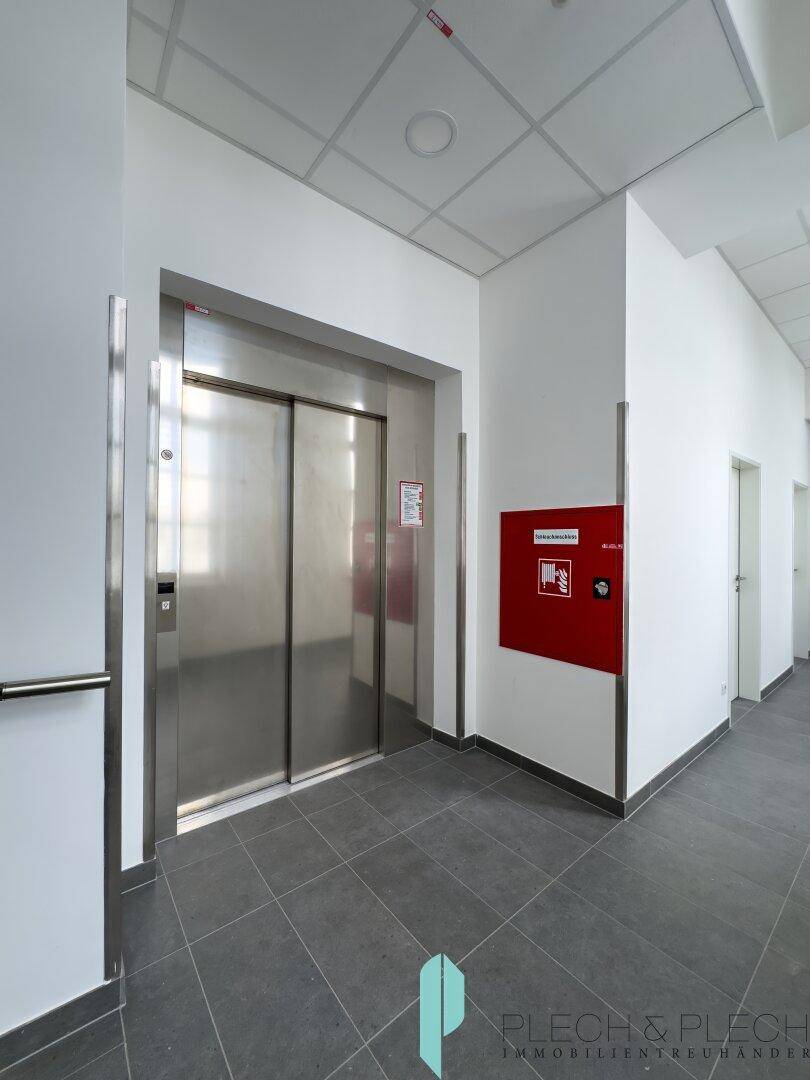 Moderner Aufzugsbereich in einem Flur mit Edelstahl-Türen und einem Brandschutzschrank.