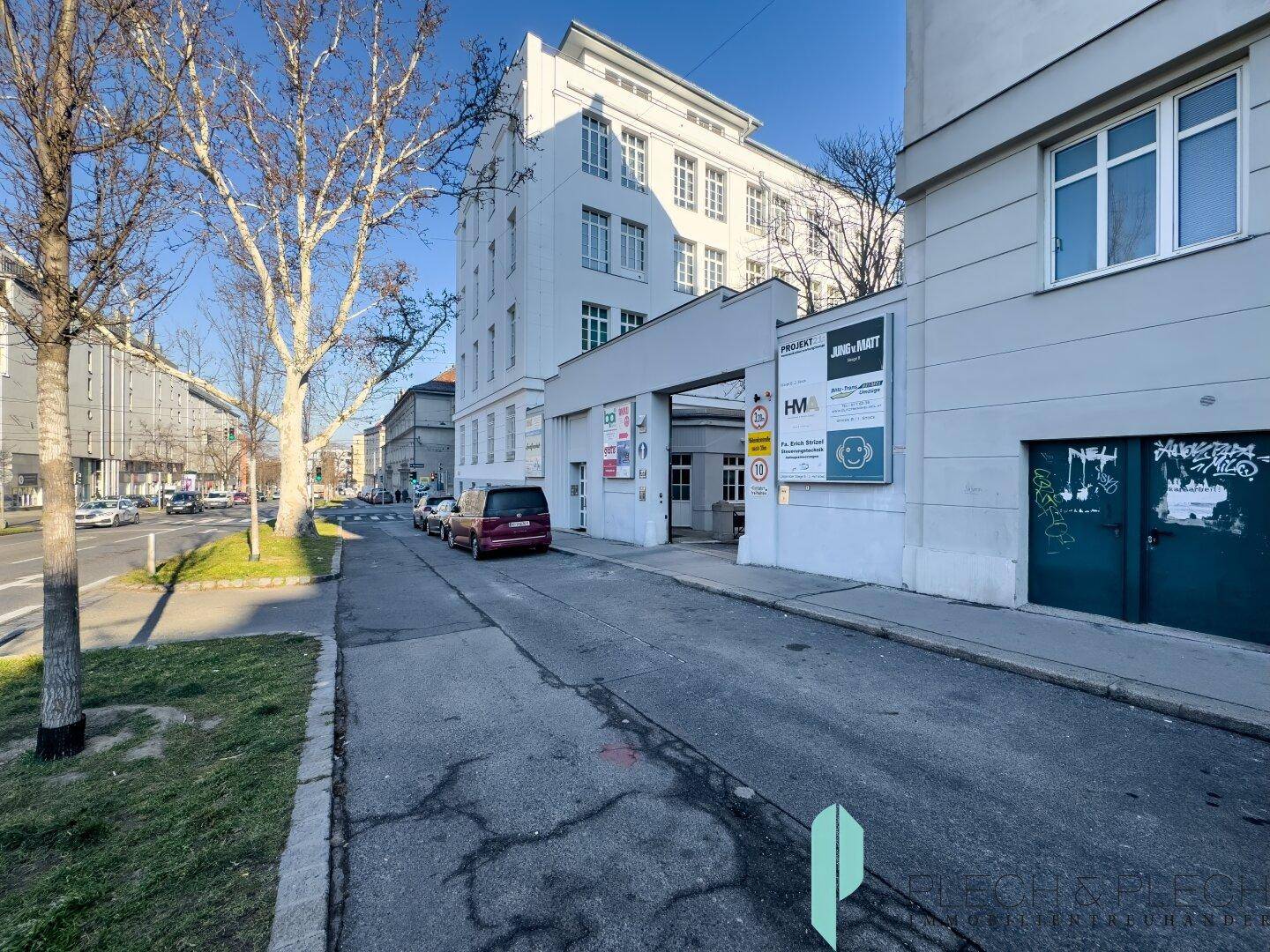 Modernes Gebäude an einer städtischen Straße mit Bäumen und geparkten Autos.