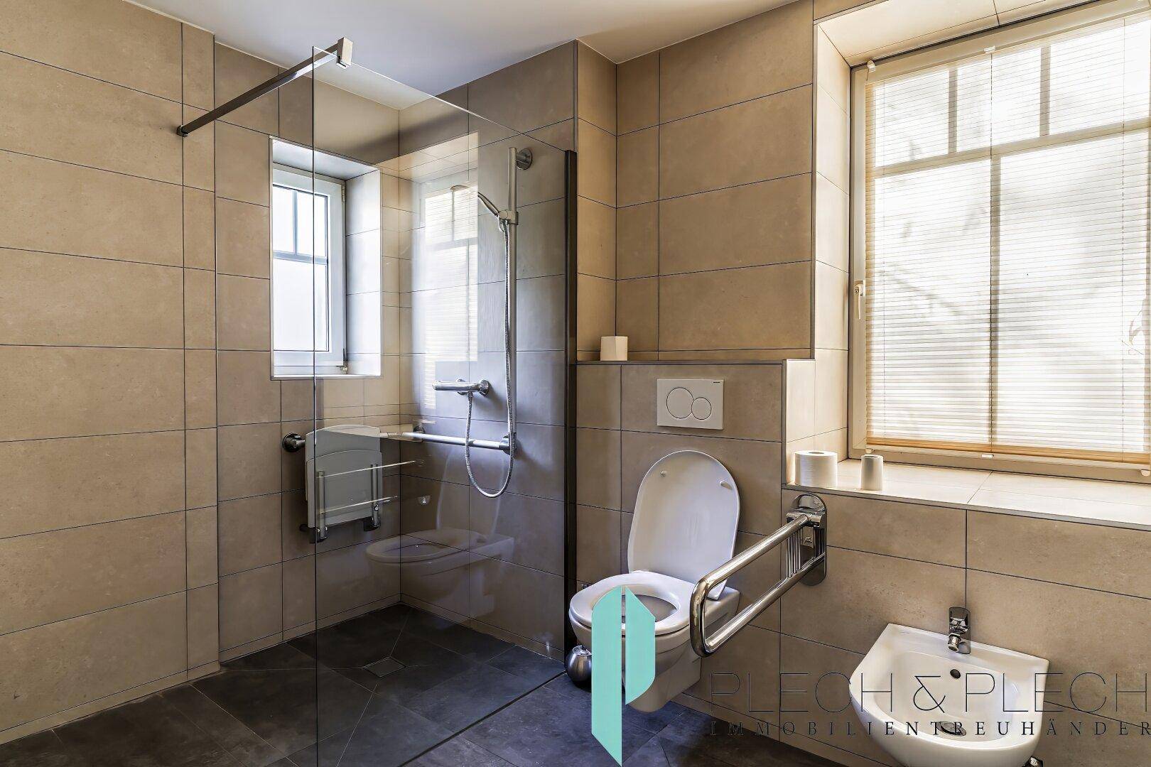 Barrierefreies Badezimmer mit Dusche, WC, Bidet und Haltegriffen.