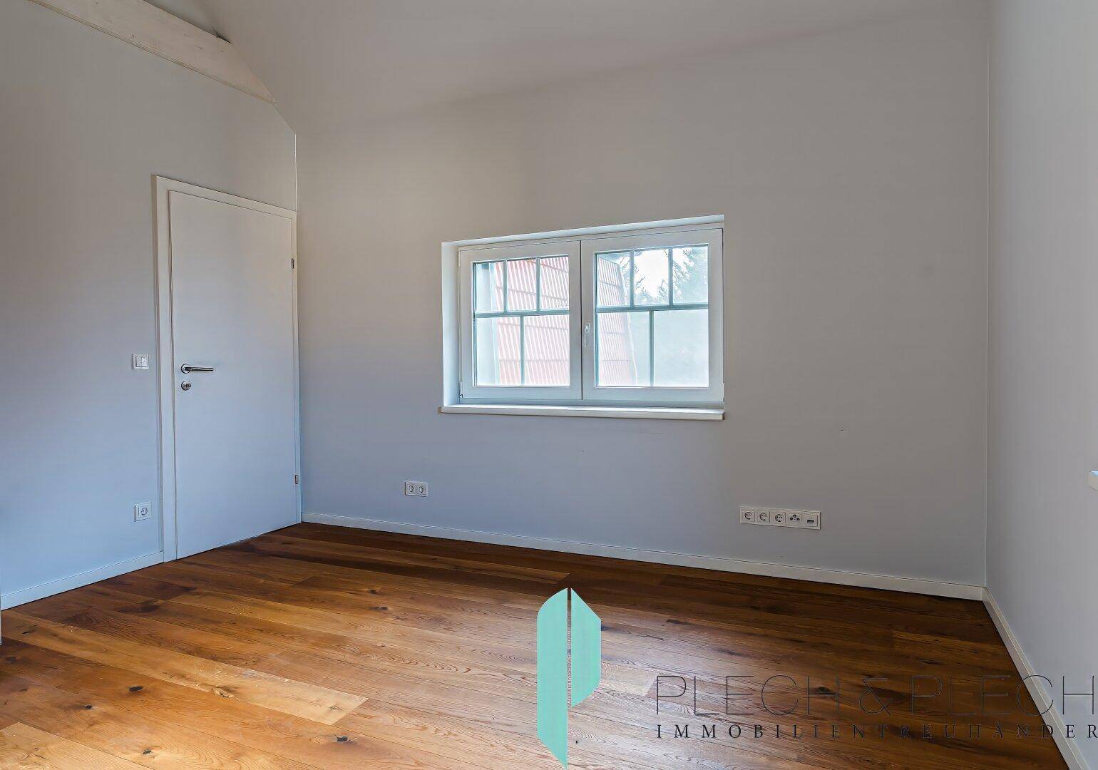 Helles Schlafzimmer mit Holzboden und einem Fenster mit Blick ins Grüne.