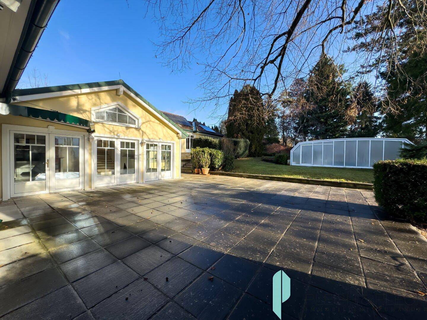 Große gepflasterte Terrasse mit Pool im Hintergrund und viel Grün.