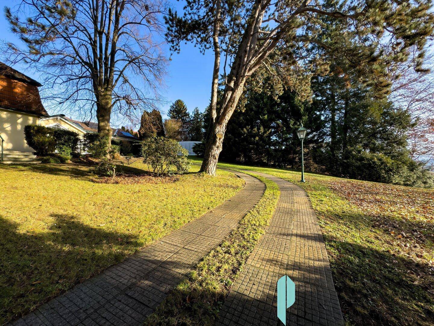 Gepflegter Gartenweg umgeben von Rasen und Bäumen unter blauem Himmel.