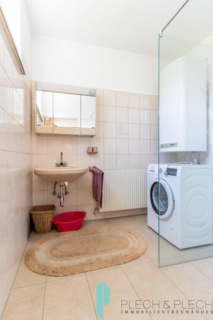 Funktionales Badezimmer mit Dusche, Waschbecken, Waschmaschine und hellen Fliesen.