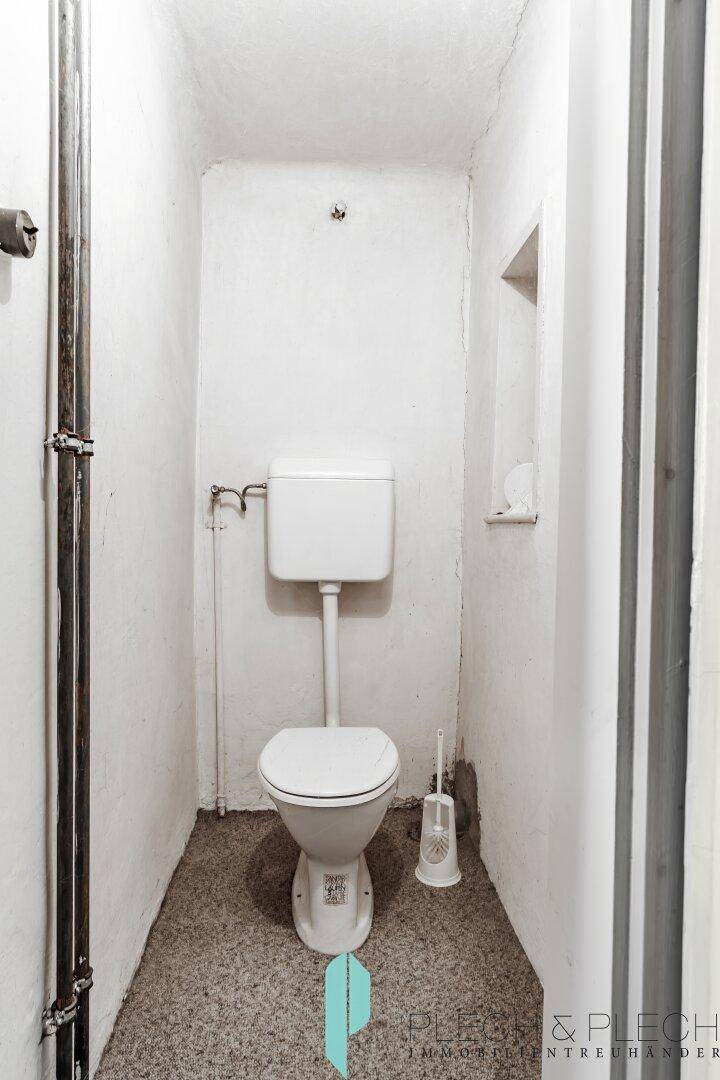 Einfache separate Toilette mit Steh-WC und gefliestem Boden in schmalem Raum.