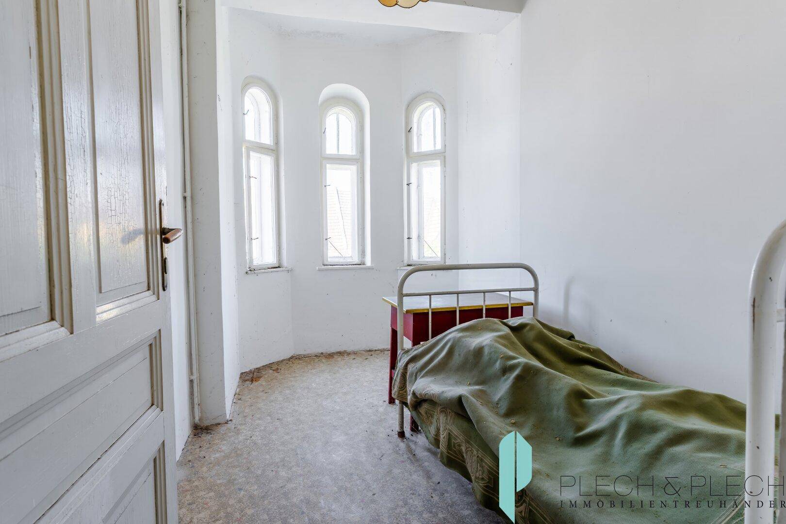 Kleines, helles Zimmer mit schmalen Fenstern und einfacher Einrichtung, ideal als Gästezimmer.