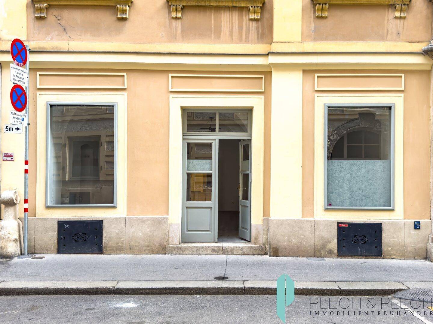 Historische Fassade eines Gebäudes mit großen Schaufenstern und einer Eingangstür zur Straße.