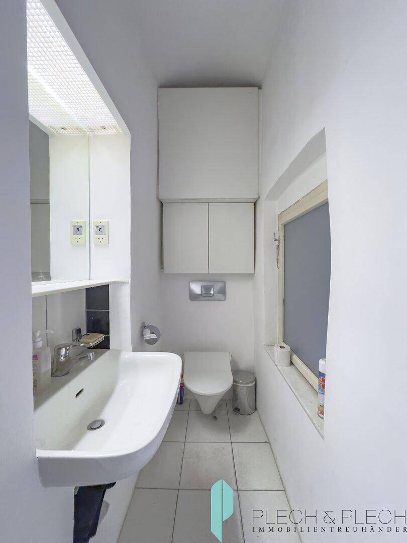 Helle Gästetoilette mit Fenster, Waschbecken, WC und weißen Fliesen.
