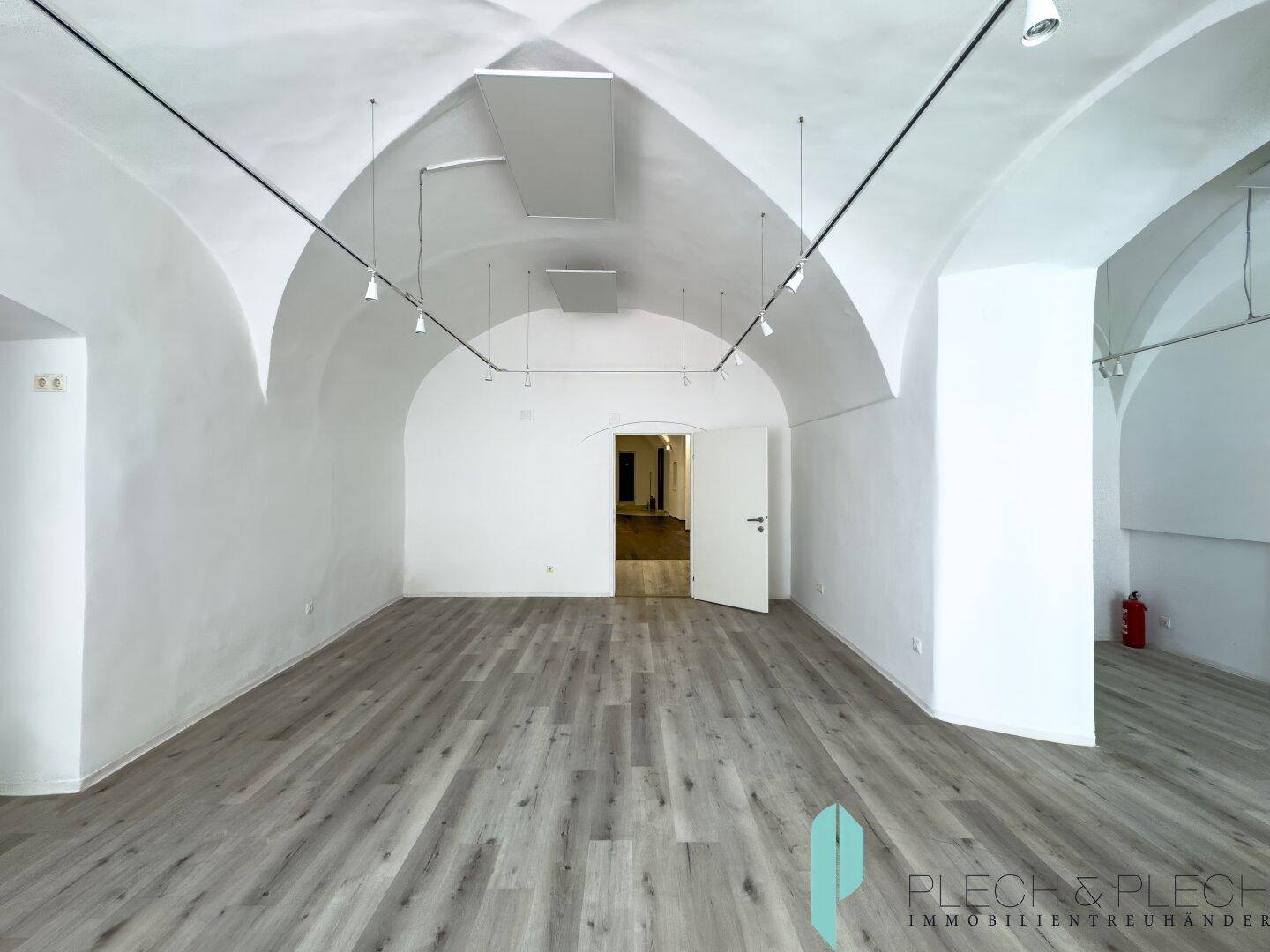 Heller Gewerberaum mit markanten Gewölbedecken, modernem Laminatboden und einem Feuerlöscher.