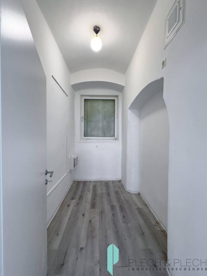 Schmaler Flur mit kleinem Fenster, hellem Laminatboden und einfacher Deckenbeleuchtung.