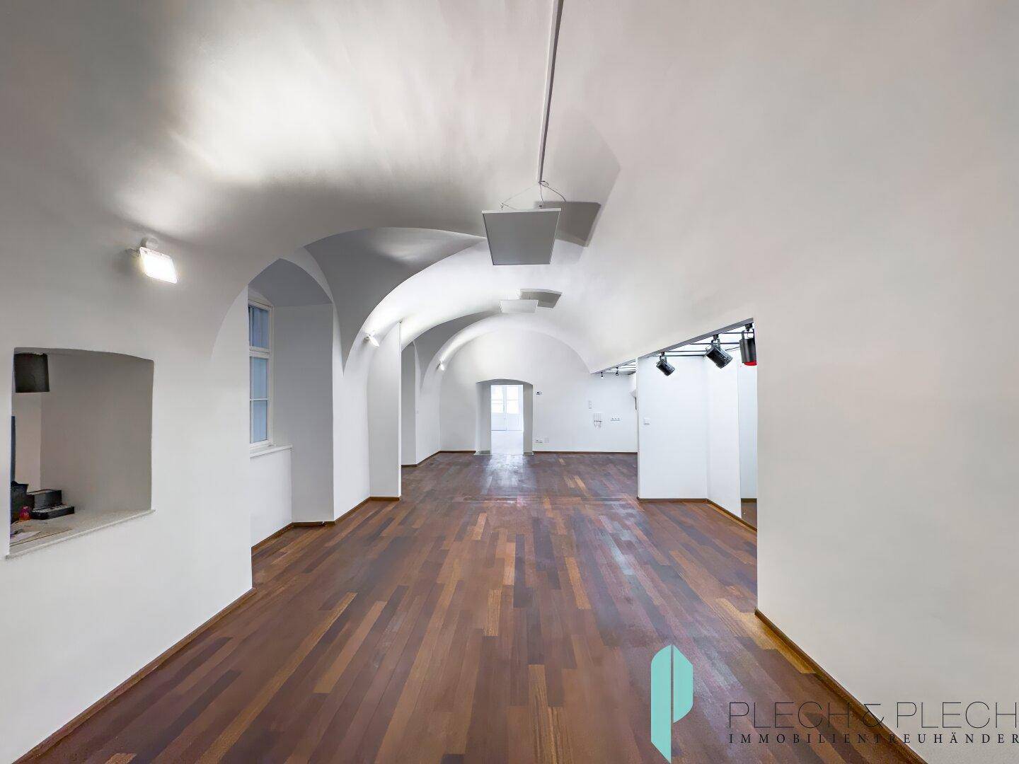 Großer Gewerberaum mit Gewölbedecken, dunklem Holzboden und indirekter Beleuchtung.