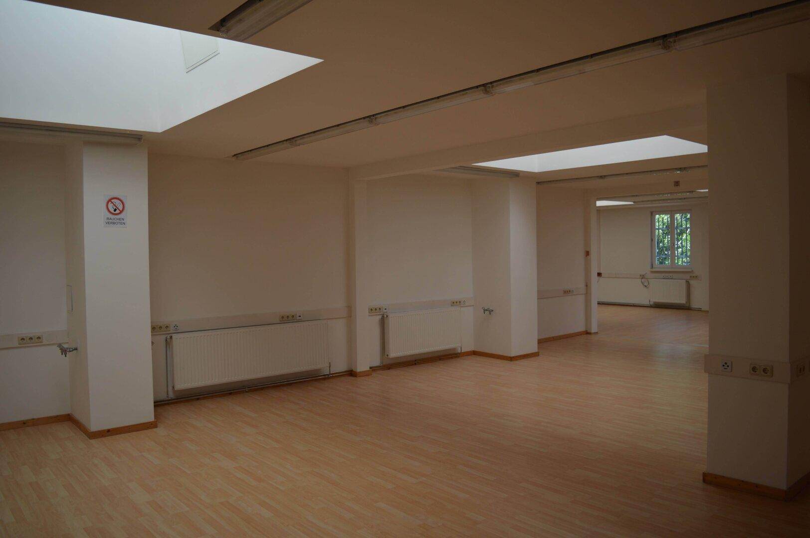 Heller, leerer Bürobereich mit Holzboden, weißen Wänden und Deckenleuchten, ideal für flexible Gestaltung.