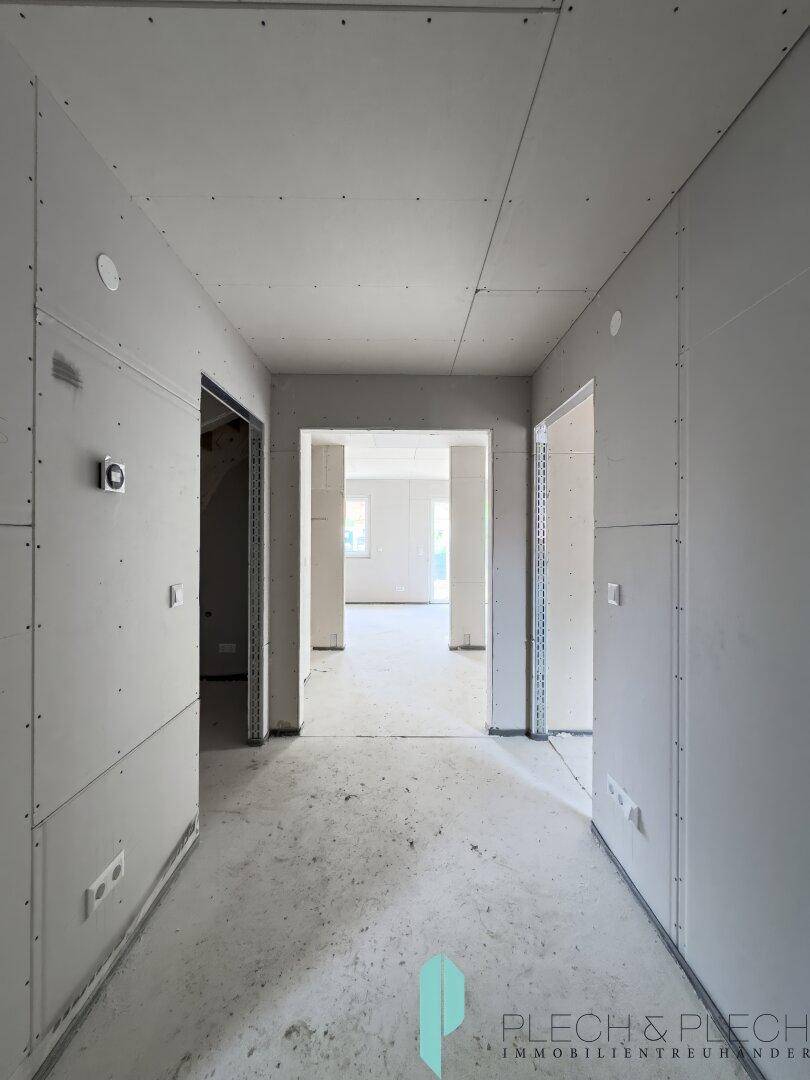 Langer Flur im Rohbau, der zu den offenen Wohnbereichen des Hauses führt.