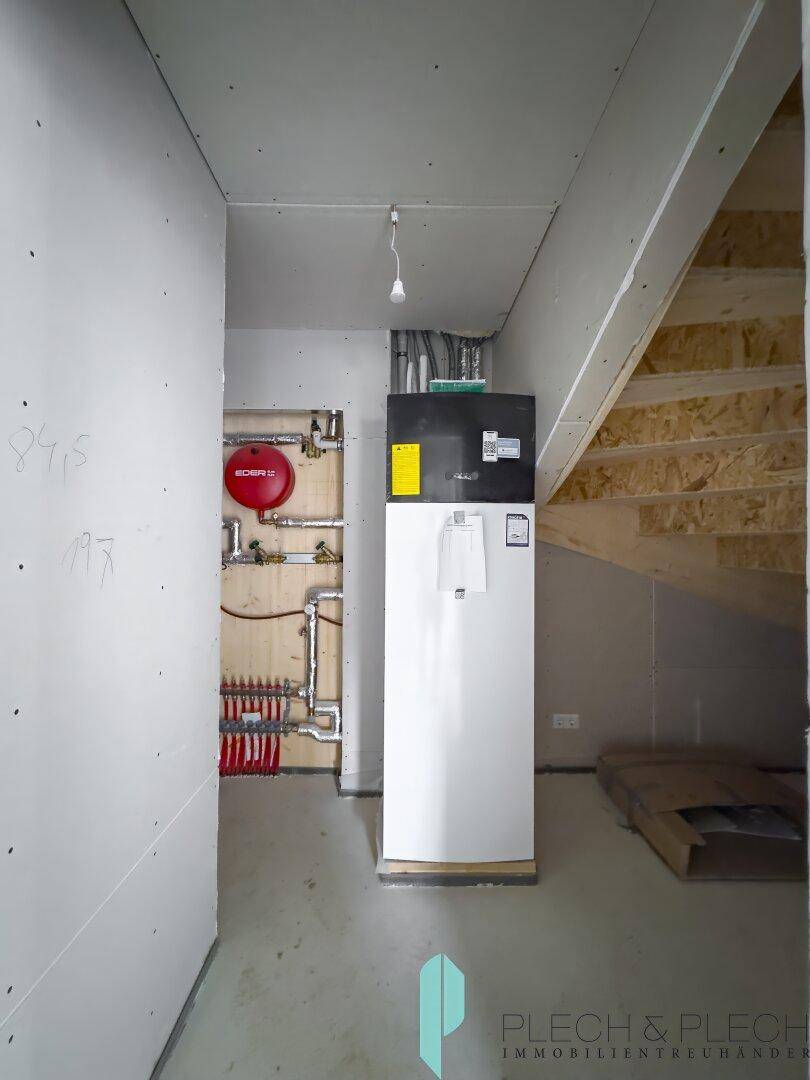 Technikraum mit Heizungsanlage und Warmwasserspeicher im Rohbauzustand.