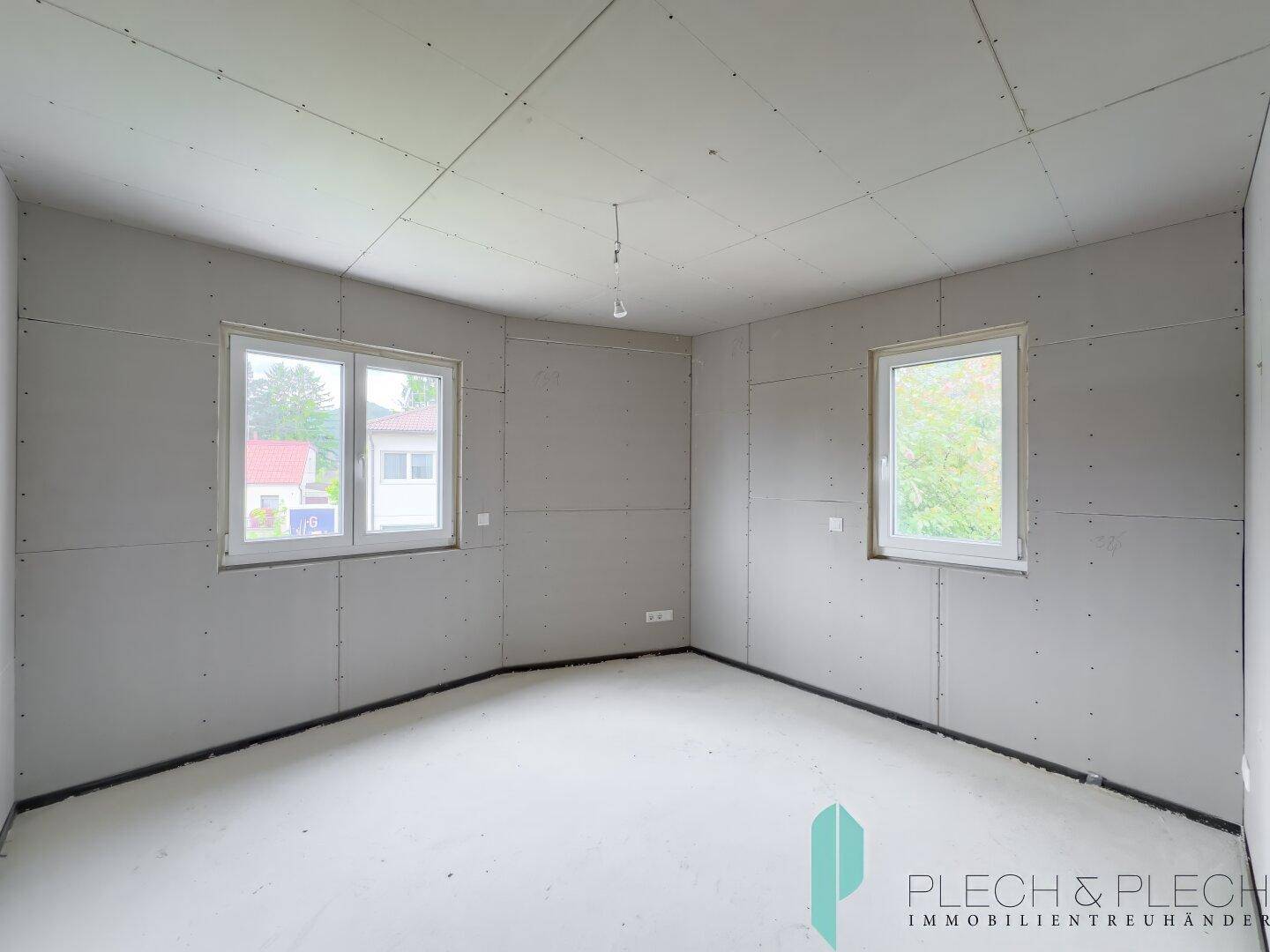 Unfertiges Schlafzimmer im Rohbau mit zwei Fenstern für viel Tageslicht.