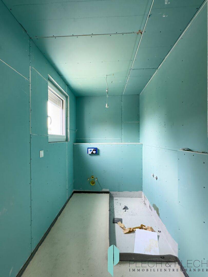 Rohbau-Badezimmer mit feuchtigkeitsbeständigen Wänden, Fenster und vorbereiteten Anschlüssen.