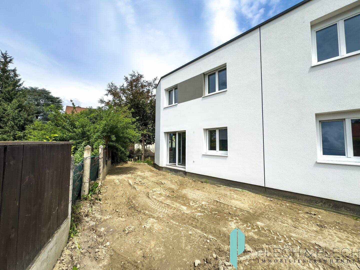 Seitenansicht des modernen Neubaus mit weißer Fassade und unfertigem Außenbereich.