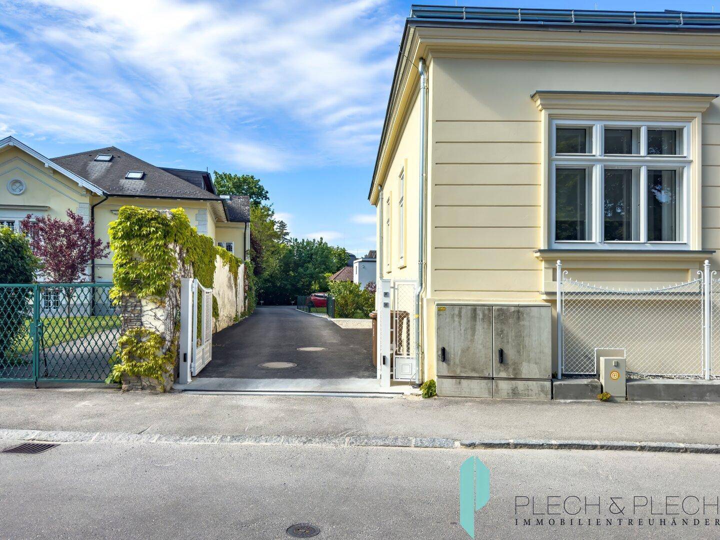 Ansicht des gelben Gebäudes von der Straße mit Einfahrt und einem weiteren Gebäude im Hintergrund.