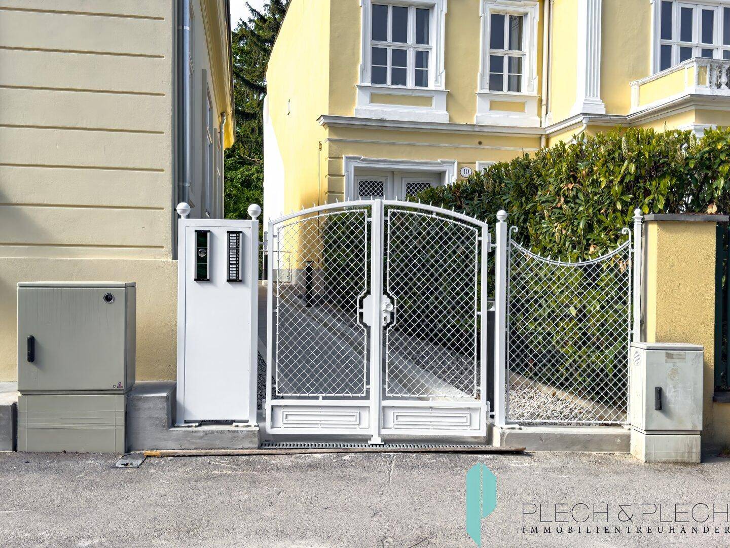 Elegantes Eingangstor mit Gegensprechanlage vor einem charmanten gelben Gebäude.