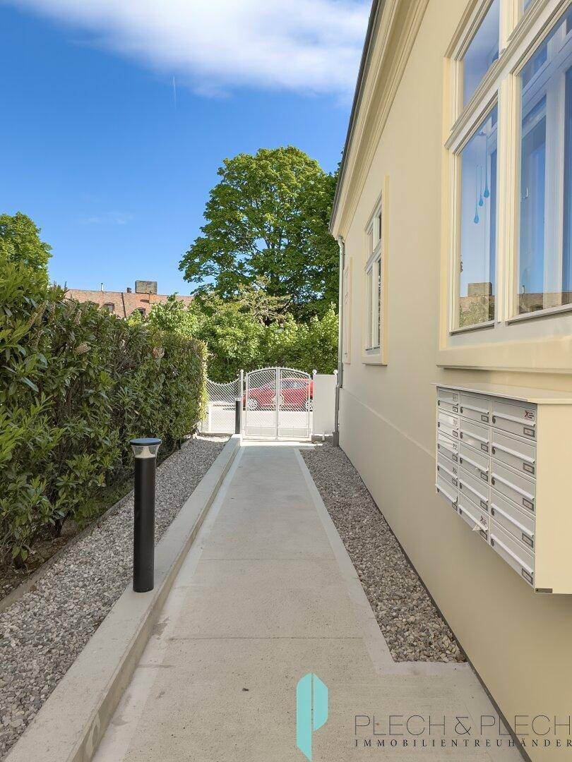 Schmaler Zugangsweg entlang der Hausfassade mit Briefkästen und Blick zum Eingangstor.