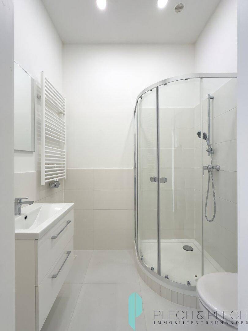 Modernes Badezimmer mit Duschkabine, Waschtisch und beheiztem Handtuchhalter in hellen Farbtönen.