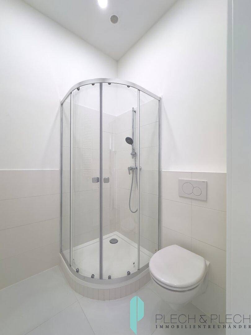 Helles Badezimmer mit moderner Duschkabine und wandhängendem WC, ausgestattet mit hellen Fliesen.
