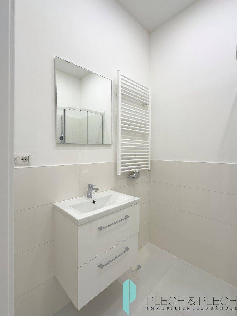 Zeitgemäßes Badezimmer mit Waschtisch, Spiegel und praktischem Handtuchheizkörper, in minimalistischem Design.