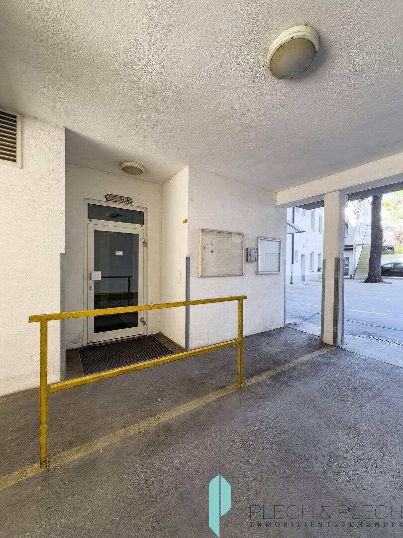 Überdachter Eingangsbereich des Gebäudes mit gelbem Geländer und Zugang zur Straße.
