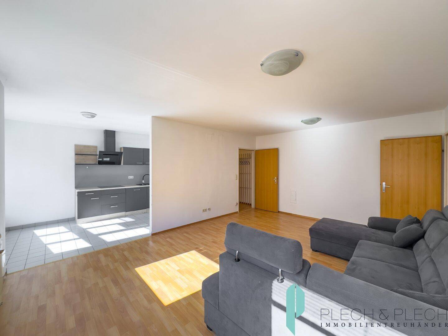 Offener Wohnbereich mit Sofa und angrenzender Küche, gekennzeichnet durch unterschiedliche Bodenbeläge.