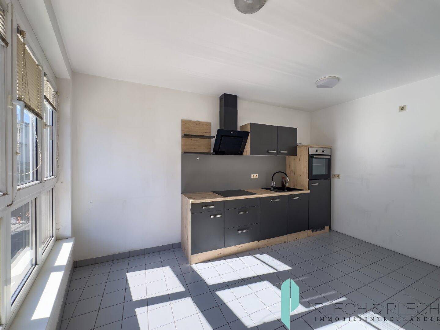 Moderne Küche mit grauen Schränken, Holzarbeitsplatte, Einbauherd und großem Fenster für viel Tageslicht.