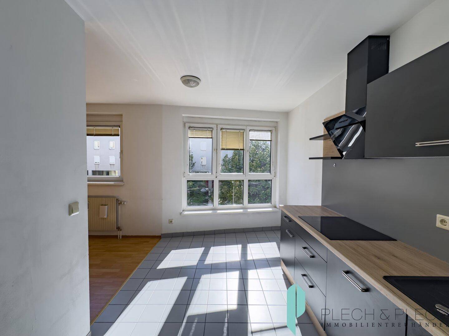 Funktionale Küche mit grauen Schränken und Induktionskochfeld, hell durch das angrenzende Fenster.