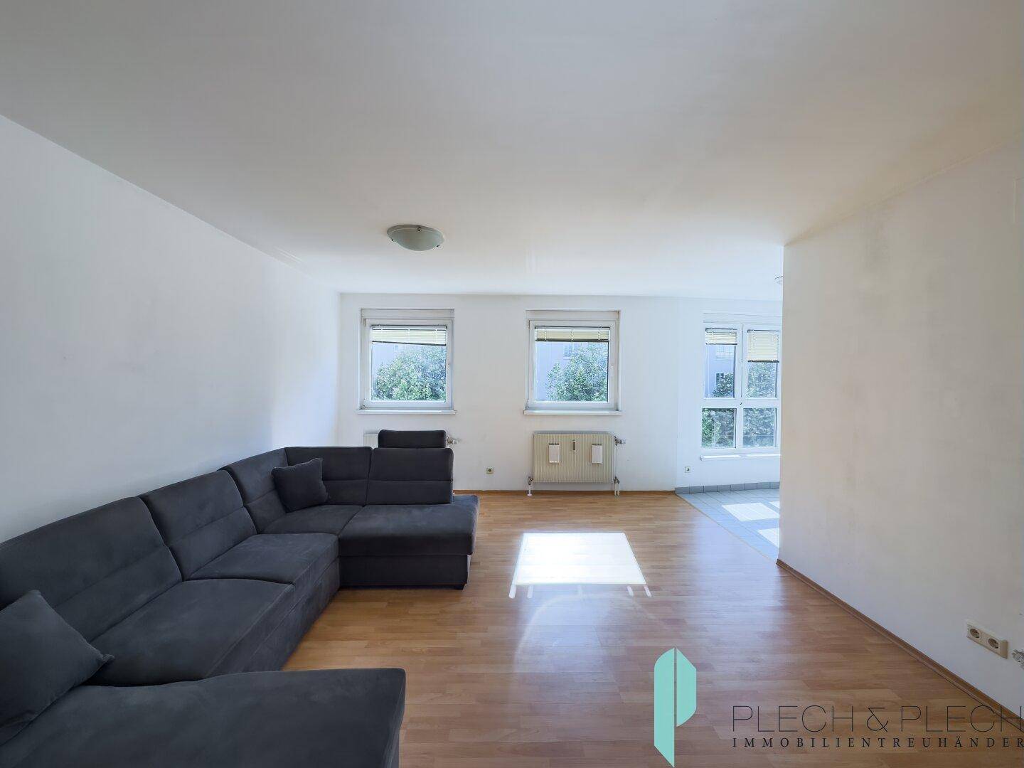 Geräumiges Wohnzimmer mit bequemer Eckcouch und hellem Parkettboden, gut beleuchtet durch mehrere Fenster.