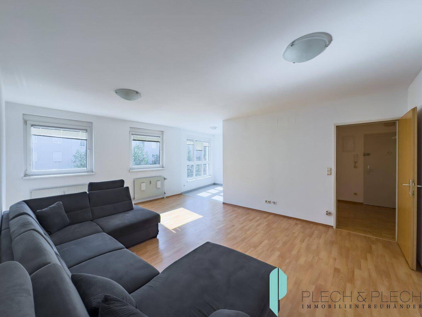 Helles Wohnzimmer mit großem Ecksofa, Parkettboden und Fenstern, die viel Tageslicht hereinlassen.