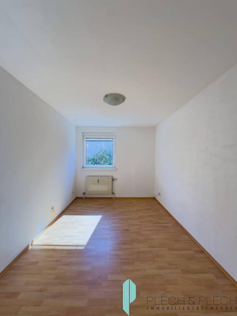 Leeres Schlafzimmer mit hellem Parkettboden und einem Fenster, das natürliches Licht in den Raum bringt.