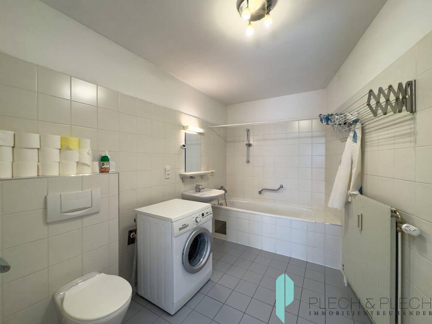 Gefliestes Badezimmer mit Badewanne, Dusche, WC und Waschmaschine, praktisch und funktional ausgestattet.