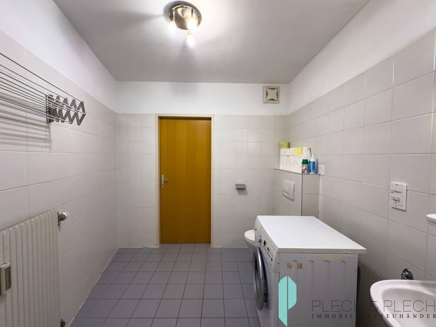 Funktionales Badezimmer mit WC, Waschmaschine und Waschbecken, komplett gefliest für einfache Pflege.