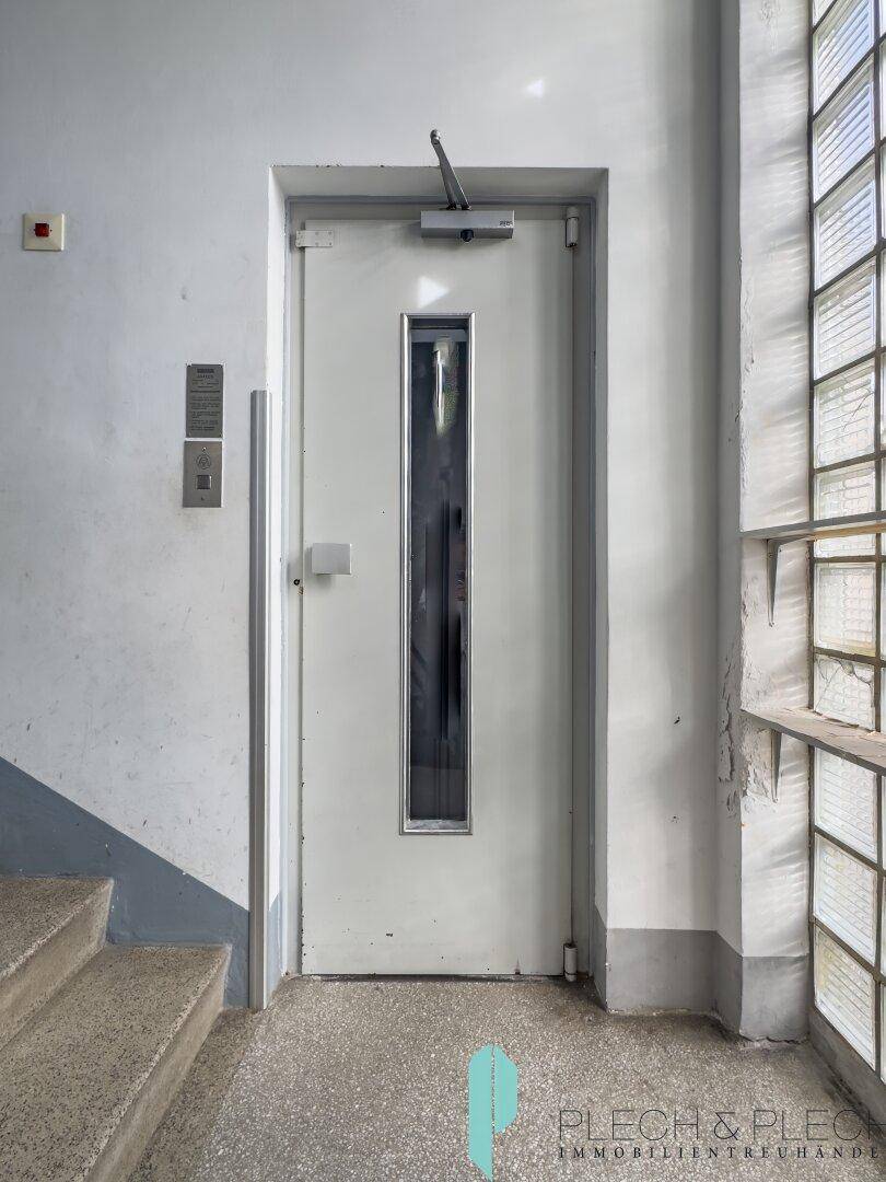 Aufzugstür im Treppenhaus mit Glasbausteinen und Treppenaufgang.