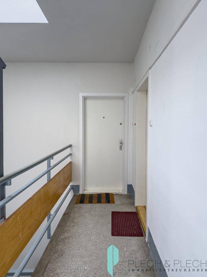 Heller Hausflur mit Treppengeländer und Eingangstür zur Wohnung.