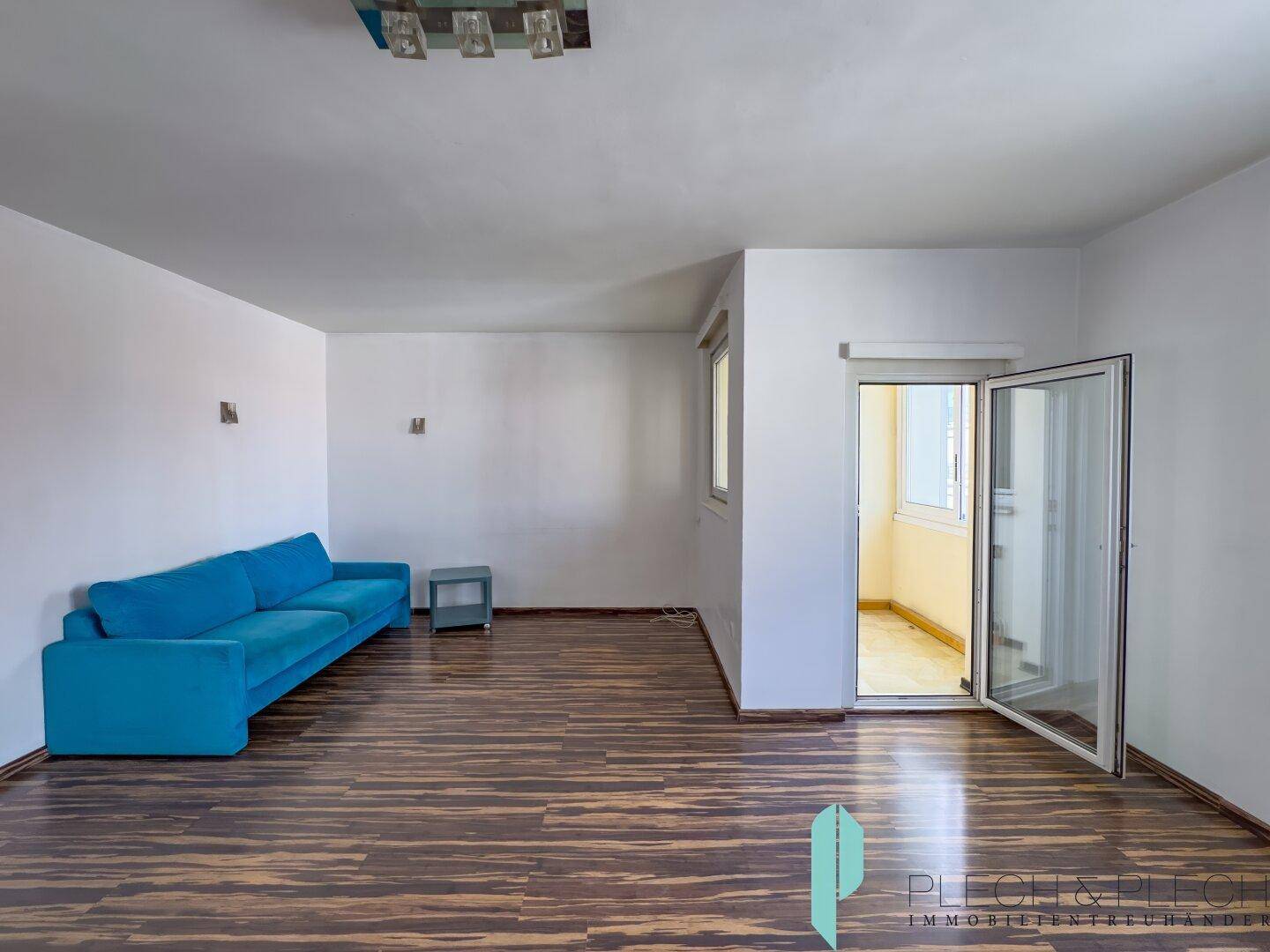 Geräumiges Wohnzimmer mit dunklem Laminatboden und offenem Zugang zu einem weiteren Raum.
